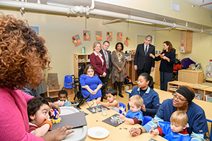 Children and the Weinberg Child Development Center, including Danny (far left), sit around a table as staff speak to HHS leaders.